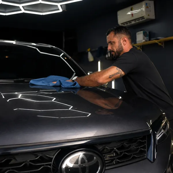 Profissional da OLJ secando o capô de um carro escuro com microfibra